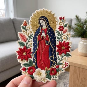 May include: An embroidered patch featuring the Virgin of Guadalupe in a red dress and blue cloak with gold stars, surrounded by a gold halo and a floral arrangement of red poinsettias, green leaves, and small white flowers on a cream background.