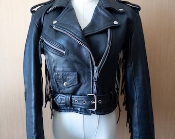 May include: A black leather jacket with fringe detailing on the sleeves and hem. The jacket has a zipper closure, a belt at the waist, and multiple pockets.