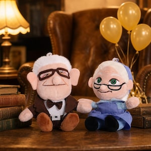 May include: Two plush dolls of animated characters, a man and a woman, sit together. The man doll wears a brown suit, bow tie, and glasses. The woman doll wears a blue dress and glasses. Yellow balloons are in the background.