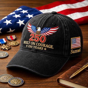 May include: Black baseball cap with an embroidered eagle design, the number 250, and the text "BUILT ON COURAGE. 250 YEARS." An American flag patch and the name "Samuel" are on the side. The cap is displayed with an American flag and medals.