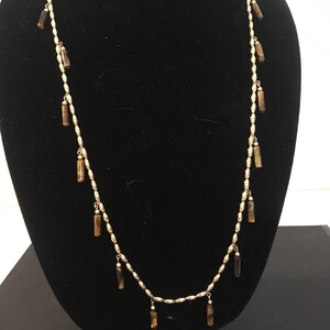 May include: A gold chain necklace with brown tiger's eye beads hanging from it. The beads are in the shape of long, thin cylinders.