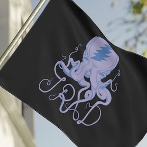 Puede incluir: Bandera negra con un diseño de pulpo morado claro y las letras "FR&D" en cursiva. El pulpo tiene un patrón de zigzag azul en la cabeza. La bandera está montada en un mástil dorado y ondea al viento.