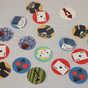 May include: A set of 15 round, colorful paper game pieces with various images, including playing cards, dominoes, and abstract designs.