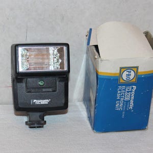 May include: A black Promatic TCL 3800 electronic flash unit with a rectangular flash head and a box. The box is blue and white with the text "Promatic TCL3200 Electronic Flash Unit".