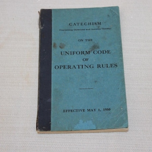 May include: A vintage softcover book titled CATECHISM ON THE UNIFORM CODE OF OPERATING RULES, EFFECTIVE MAY 1, 1950. The cover is light blue with a dark blue spine and black text. The surface shows signs of age with minor dark spots and wear.