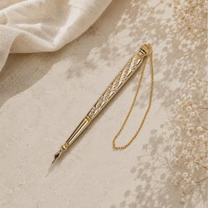 May include: A gold-toned metal pen featuring a spiraling inlay of clear, sparkling crystals along its barrel. The pen includes a slender gold chain attached to the top cap and a pointed, metallic nib at the writing end, finished with a polished surface.