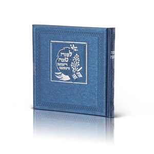 May include: A square, deep blue book with a textured cover featuring a silver embossed square frame. Inside the frame is a silver graphic of a pomegranate and Hebrew text. The spine of the book also displays silver Hebrew lettering.