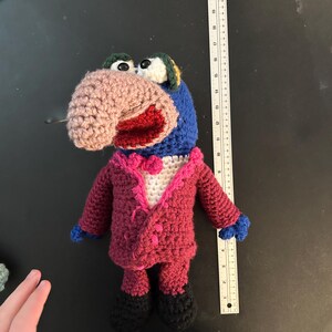 Pu&ograve; includere: Bambola all'uncinetto fatta a mano di un personaggio dei Muppet, con naso rosa, testa blu e abito rosso con papillon bianco. La bambola ha scarpe nere e mani blu. La bambola &egrave; alta circa 25 cm.
