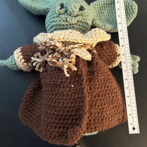 May include: Crocheted doll of a character with large ears, green skin, and a brown coat. The doll is approximately 10 inches tall. The doll's coat has a tan collar and is made of brown yarn. The doll is handmade.