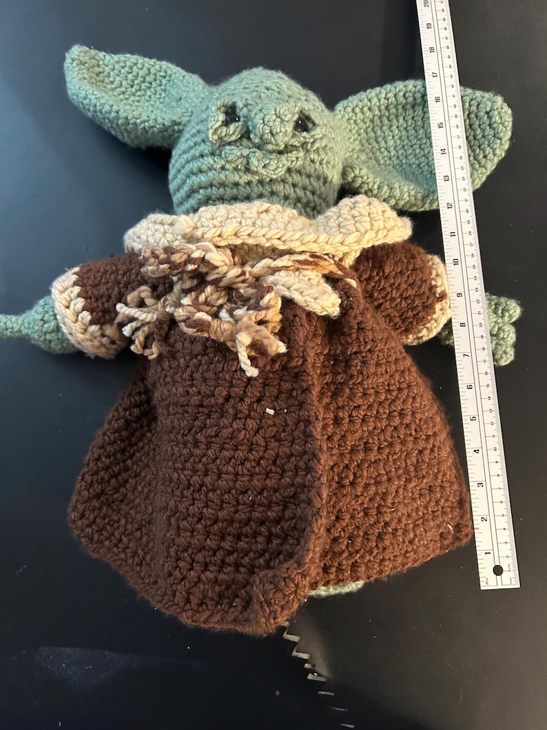May include: Crocheted doll of a character with large ears, green skin, and a brown coat. The doll is approximately 10 inches tall. The doll's coat has a tan collar and is made of brown yarn. The doll is handmade.