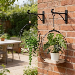 May include: Two black metal hanging planters with wooden shelves and spherical wooden beads. One holds a trailing green plant, the other a large-leafed plant. The planters are mounted on a red brick wall.