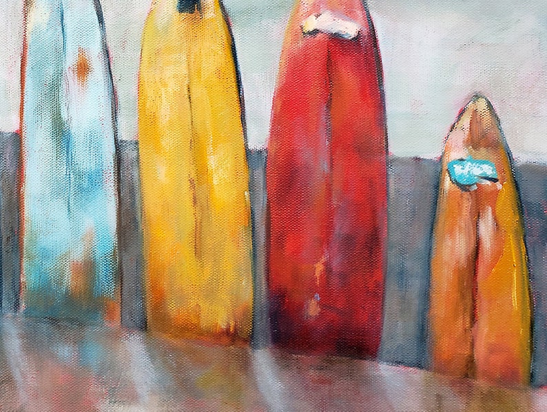May include: Four vintage surfboards lined up on a beach, painted in shades of blue, yellow, red, and orange. The surfboards have a worn, weathered look, suggesting they have been used many times.