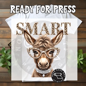 May include: White t-shirt with a graphic of a donkey wearing glasses and a pearl necklace. The word "SMART" is printed above the donkey in a leopard print font. The text "READY FOR PRESS" is at the top.
