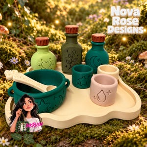 May include: A set of silicone play items including a dark green cauldron with a cream spoon, three small bottles with brown caps, and three small cups in green, cream, and pink. Each piece features embossed icons like hearts, stars, and moons.