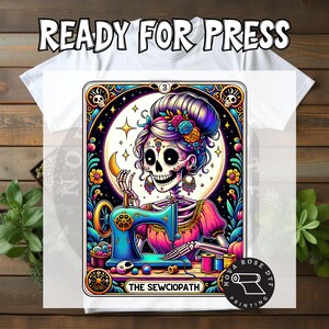 May include: A white t-shirt featuring a colorful graphic of a skeleton with a floral updo using a blue sewing machine. The design includes the text "THE SEWCIOPATH" at the bottom and "READY FOR PRESS" at the top, surrounded by ornate borders.