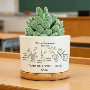 Puede incluir: Una taza de cerámica blanca con asa negra y el texto "But First, Coffee" en negrita negra. La taza se encuentra sobre un fondo borroso, sugiriendo un ambiente acogedor.