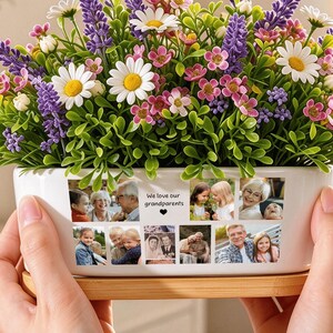 May include: A white rectangular ceramic planter with a bamboo base, filled with artificial lavender, daisies, and pink flowers. The front of the planter features a collage of six small family photographs and the text "We love our grandparents".