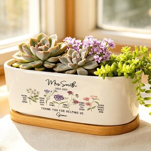 May include: A rectangular white ceramic planter with a bamboo base, filled with succulents and small purple flowers. The planter has the text "Mrs. Smith 2024-2025" and "THANK YOU FOR HELPING US Grow" with student names and floral illustrations.