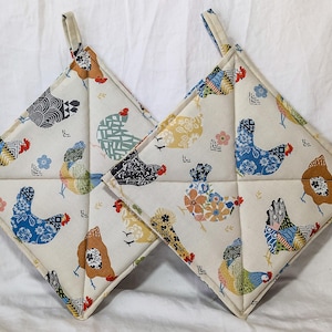 May include: Two square pot holders with a cream background and a repeating pattern of colorful chickens. The chickens are in various colors and patterns, including blue, orange, and black. Each pot holder has a loop for hanging.