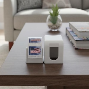 May include: A dark brown square coffee table with a white tissue box and a small stamp dispenser with American flag stamps. A gray sofa with patterned pillows is in the background. A stack of books and a small plant are also on the table.