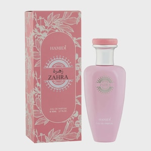 May include: A pink perfume bottle and matching box. The box is decorated with white floral patterns and the brand name "HAMIDI". The bottle has a silver neck and a pink cap. The text "ZAHRA" is displayed on both the bottle and the box. The bottle contains 2.7 fl oz of perfume.