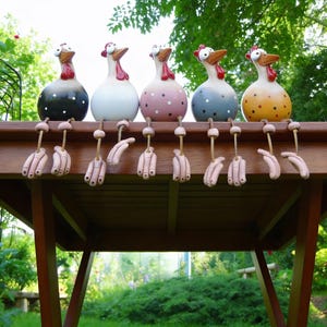 Può includere: Cinque fantasiose statuette di gallina in ceramica con corpi colorati e creste rosse sono appollaiate su un tavolo di legno. Ogni gallina ha una combinazione di colori unica, tra cui nero con pois bianchi, bianco, rosa con pois bianchi, blu con pois bianchi e giallo con pois marroni. Le loro gambe sono mani penzolanti.