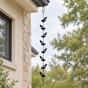May include: A black metal rain chain featuring a series of eight small bird figures perched on individual circular basins, connected by a vertical link chain and suspended from an S-hook attached to the edge of a building roofline.