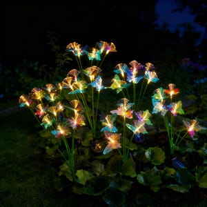 May include: A display of vibrant, illuminated fibre optic flowers in a garden. The flowers, resembling butterflies, display a range of colours such as blue, yellow, and orange. The stems are green, and the scene is illuminated at night.