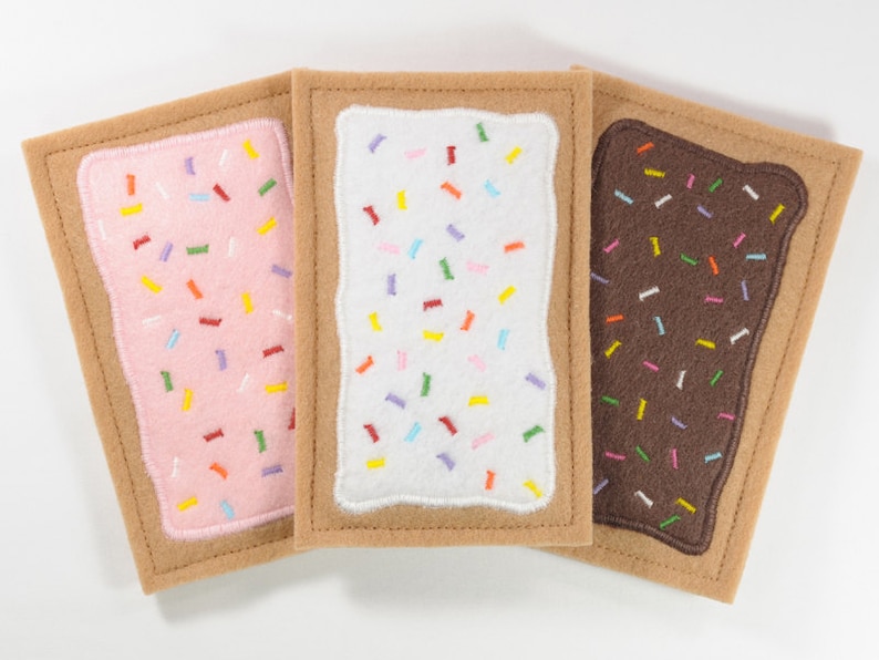 May include: Three felt squares resembling a popular breakfast pastry. The squares are brown, pink, and white with colorful sprinkles on top.