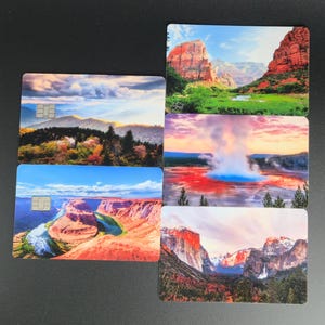 May include: A collection of five rectangular cards featuring scenic landscape images. The cards display various natural scenes, including mountains, canyons, and geysers, with vibrant colors and detailed imagery. Each card has a small, embedded chip.