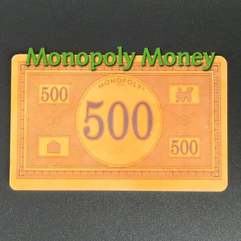 May include: A Monopoly money bill with a value of 500. The bill is orange with the text "Monopoly Money" in green at the top. The number 500 is prominently displayed in a large circle in the center.
