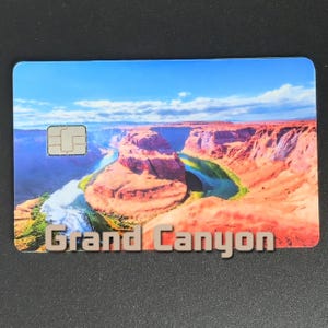 May include: A rectangular card featuring a scenic view of the Grand Canyon under a blue sky. The card displays the text "Grand Canyon" in a 3D font. A small chip is visible on the upper left corner.
