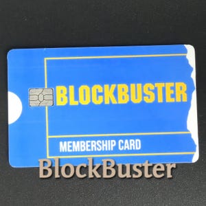 May include: A blue Blockbuster membership card with yellow text and a white circle on the left side. The card reads "BLOCKBUSTER" and "MEMBERSHIP CARD". A smaller Blockbuster logo is below the card.