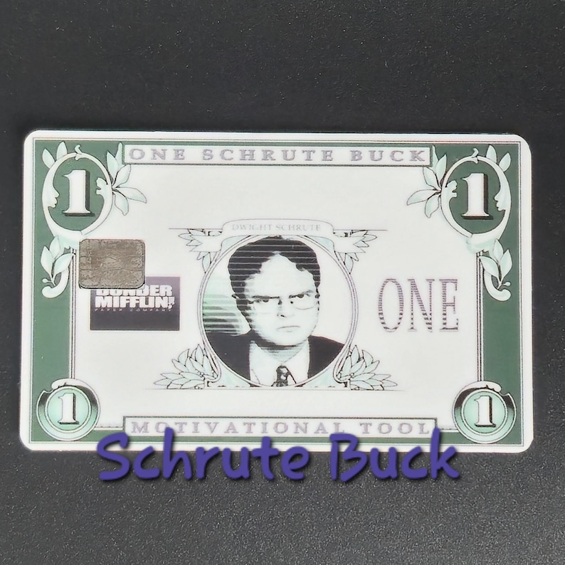 May include: A novelty item resembling a one-dollar bill, featuring a portrait of Dwight Schrute. The design includes the text "ONE SCHRUTE BUCK" and "MOTIVATIONAL TOOL". The item is green and white.