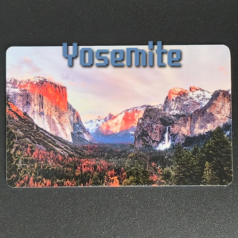 May include: A rectangular magnet featuring a scenic view of Yosemite National Park. The image showcases towering mountains, a waterfall, and a vibrant forest, with the word "Yosemite" in blue letters at the top.