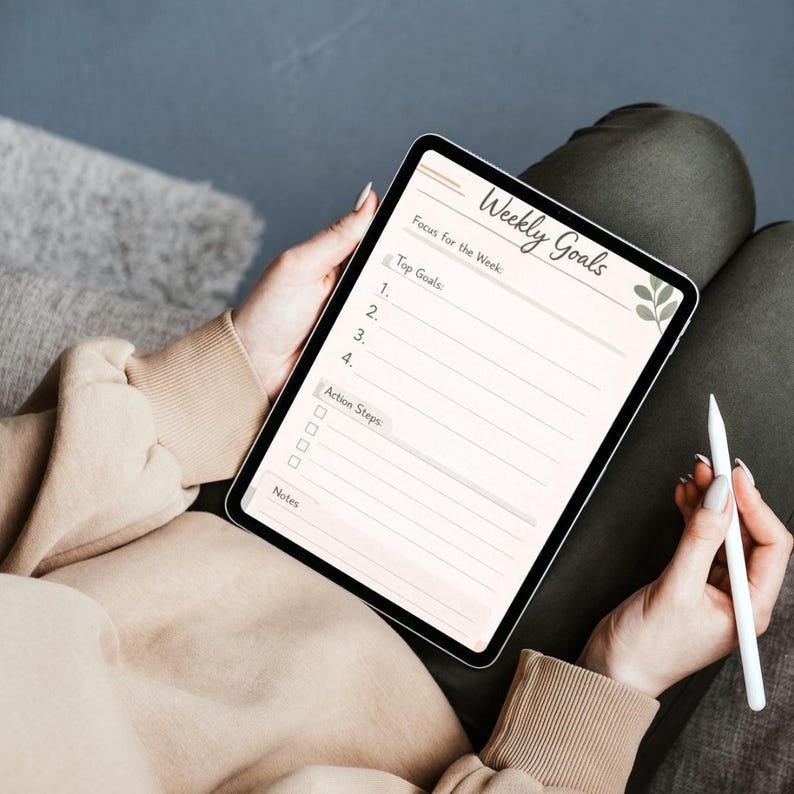 May include: A digital tablet displaying a Weekly Goals planner template with sections for Top Goals, Action Steps, and Notes. The interface features a soft beige background, dark text, and a small green leaf illustration on the right side.