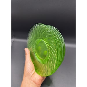 May include: A stack of translucent lime green glass saucers featuring a radial swirl pattern that radiates from the center to the outer rim. The glass has a smooth, glossy finish and a circular shape, showcasing a vibrant, light-catching color.