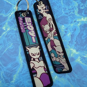 May include: Two black keychains with silver rings. Each keychain features a design of the character Mewtwo from the Pokémon series. One keychain has the text "Mewtwo" in English and Japanese. The other keychain has a Mewtwo graphic.