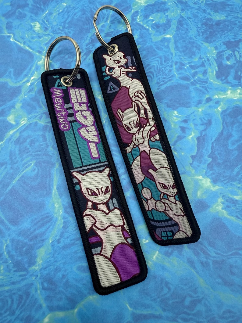 May include: Two black keychains with silver rings. Each keychain features a design of the character Mewtwo from the Pok&eacute;mon series. One keychain has the text "Mewtwo" in English and Japanese. The other keychain has a Mewtwo graphic.
