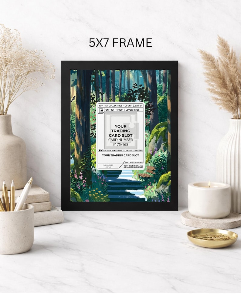 May include: A black 5x7 frame displaying a forest scene with a path and a trading card slot. The card slot has text that reads "YOUR TRADING CARD SLOT CARD NUMBER #175/165". The frame is on a white surface.