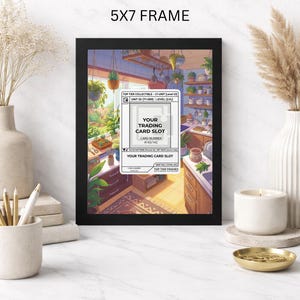 May include: A black 5x7 frame with a colorful illustration of a kitchen scene. The artwork includes text that reads "YOUR TRADING CARD SLOT" and "TOP TIER FRAMES". The frame is displayed on a white marble surface.