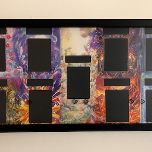 Puede incluir: Marco de exhibici&oacute;n negro con m&uacute;ltiples aberturas rectangulares. El fondo presenta coloridas obras de arte florales y fant&aacute;sticas. El marco es rectangular y est&aacute; montado en una pared blanca.