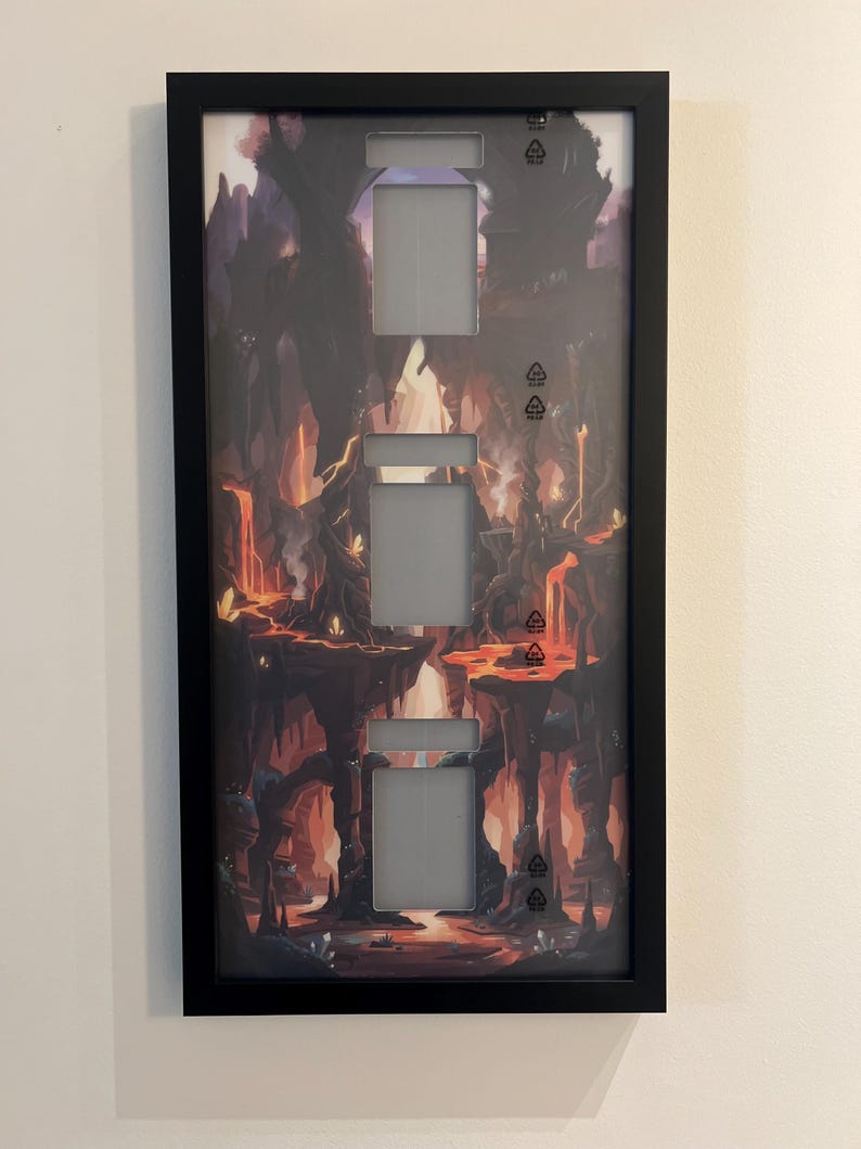 Puede incluir: Una cubierta de interruptor de luz enmarcada en negro con un dise&ntilde;o de paisaje de fantas&iacute;a. La obra de arte presenta una escena cavernosa y ardiente con lava y formaciones rocosas. Tiene tres aberturas para interruptores.