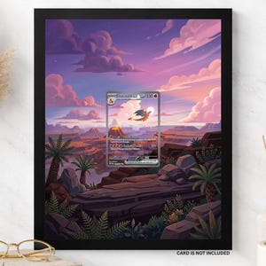 May include: A black 8x10 frame containing a landscape print of a sunset over a canyon with a Charizard trading card centered in the middle. The print features purple and orange clouds, rocky terrain, and palm trees. Text reads 8X10 FRAME.