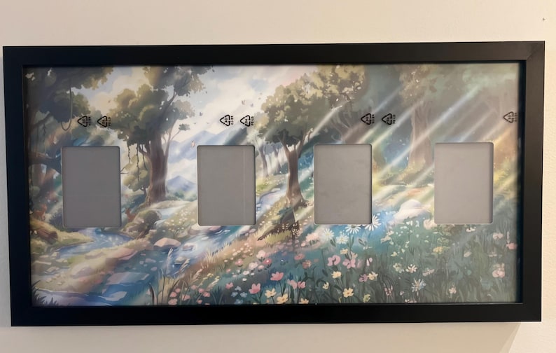 May include: A black rectangular picture frame with four openings. The background art depicts a forest scene with trees, a stream, and flowers. The frame is mounted on a white wall.