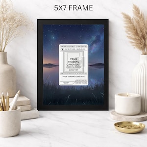 May include: A black 5x7 frame displaying a trading card slot with the text "YOUR TRADING CARD SLOT CARD NUMBER #202/197". The background features a scenic landscape with a starry sky and water. The frame is on a white surface.