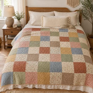May include: A bed featuring a patchwork quilt in shades of pink, blue, green, and yellow. Some squares of the quilt have a floral pattern. The bed is dressed with white pillows and a decorative fringed cushion.