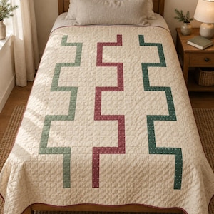 Könnte beinhalten: Eine cremefarbene Steppdecke mit einem geometrischen Muster aus drei vertikalen, treppenartigen Linien in gedecktem Grün und Dunkelrot. Der Stoff weist eine feine, gesprenkelte Textur auf und ist an den Rändern mit einer schmalen roten Einfassung versehen.