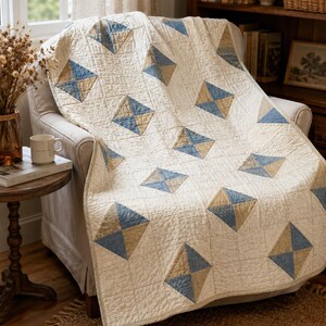 May include: A quilted throw blanket featuring a repeating pattern of cream-coloured squares interspersed with diamond-shaped blocks. Each diamond is divided into four triangles, alternating between muted blue and tan fabric, with visible stitching.