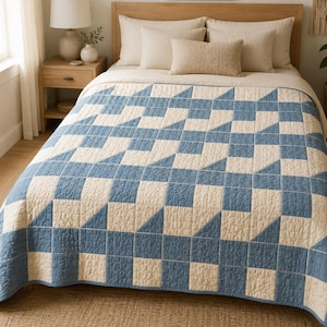 May include: A quilt featuring a geometric pattern of alternating blue and cream-colored squares and triangles. The fabric has a visible quilted texture with stitched lines forming the shapes across the entire surface of the bedding.
